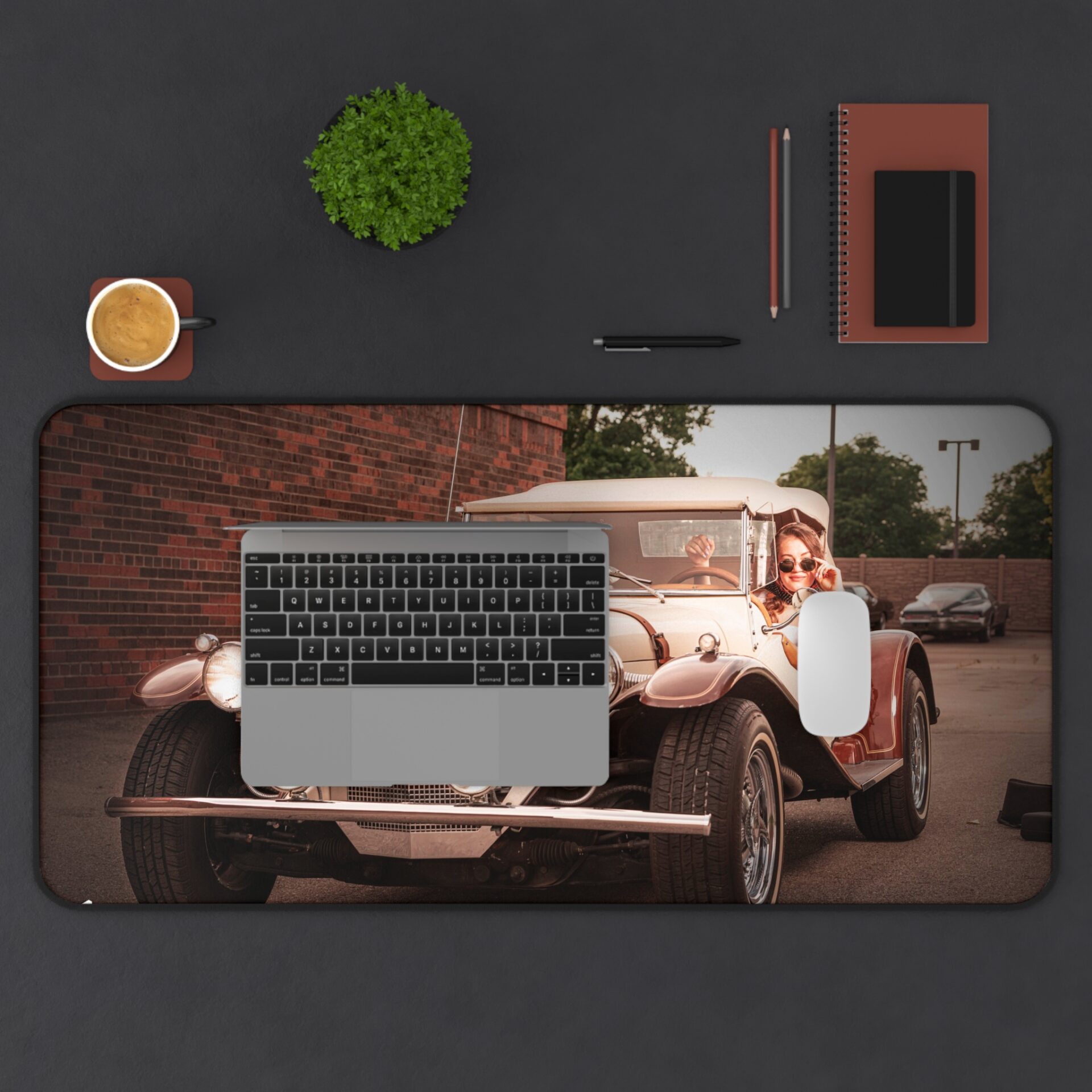 A laptop on a large desk mat featuring a vintage car and woman.