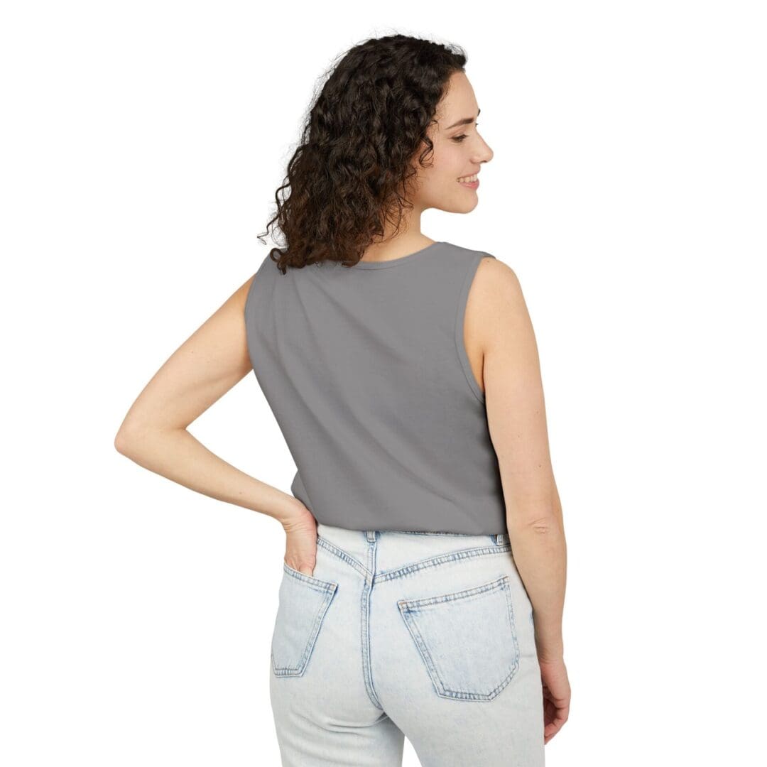 Woman in a gray sleeveless top and light blue jeans, posing with her back to the camera.