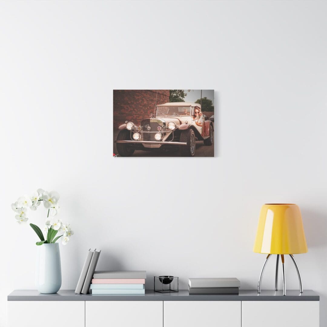 Vintage car photo mounted above modern sideboard with lamp and flowers.