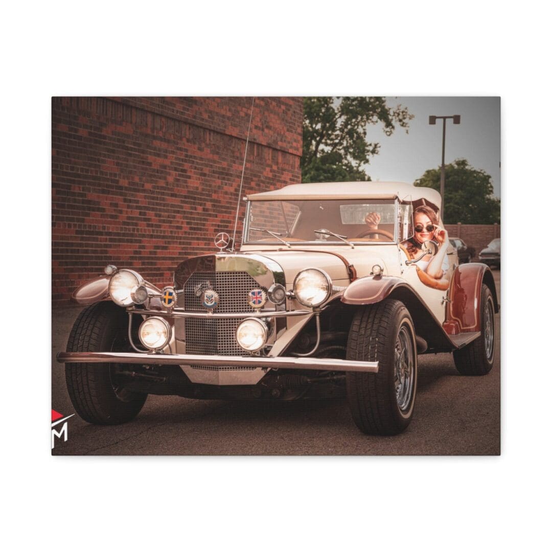 A vintage car with a person inside parked by a brick wall.