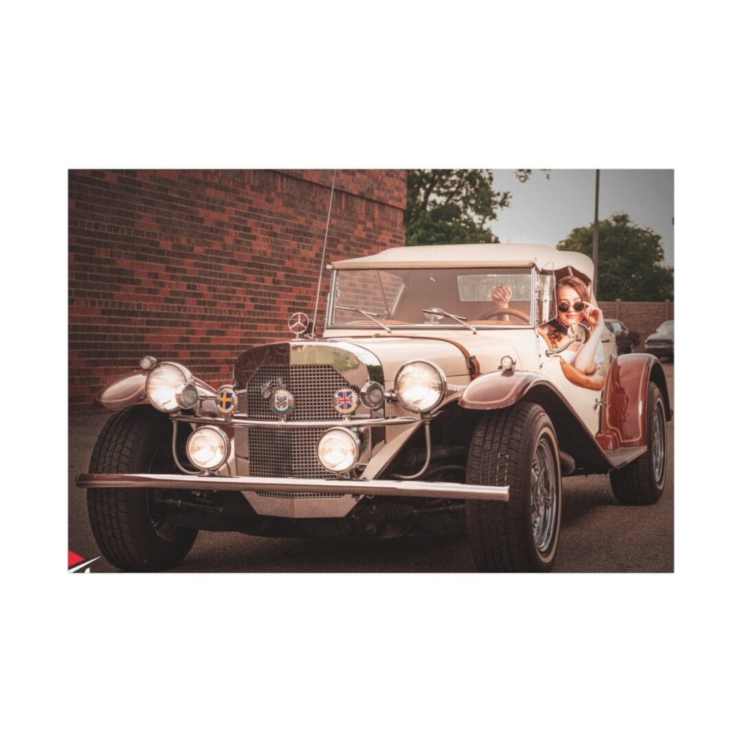 A vintage car with a driver and passenger in front of a brick building.