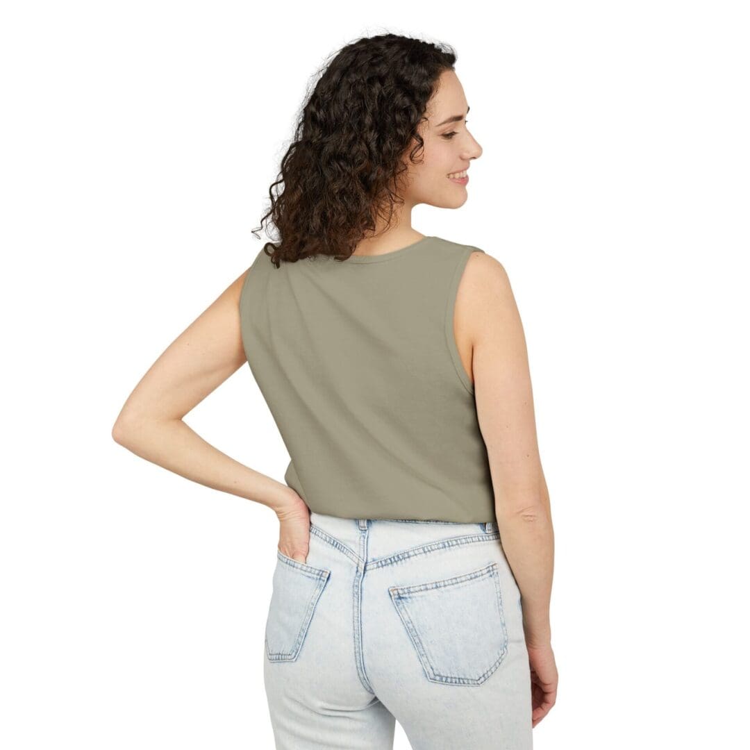 Woman wearing a sleeveless olive green top and light blue jeans, posing with her back to the camera.